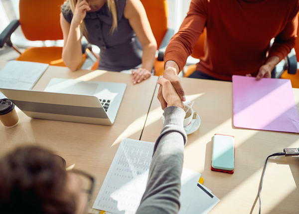 recruiters and interviewee shaking hands over table with coffees and laptop