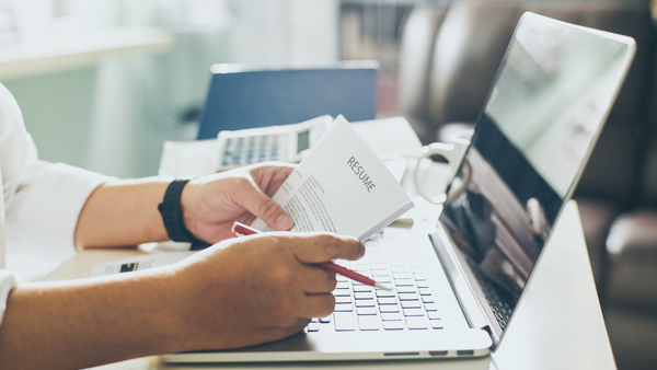 recruiter looking over received resume at laptop holding red pen