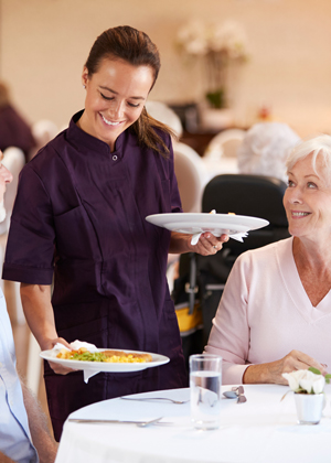 care assistant serving meals in nursing home to residents