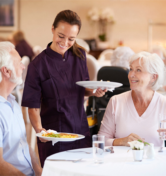 care assistant serving meals in care home to residents